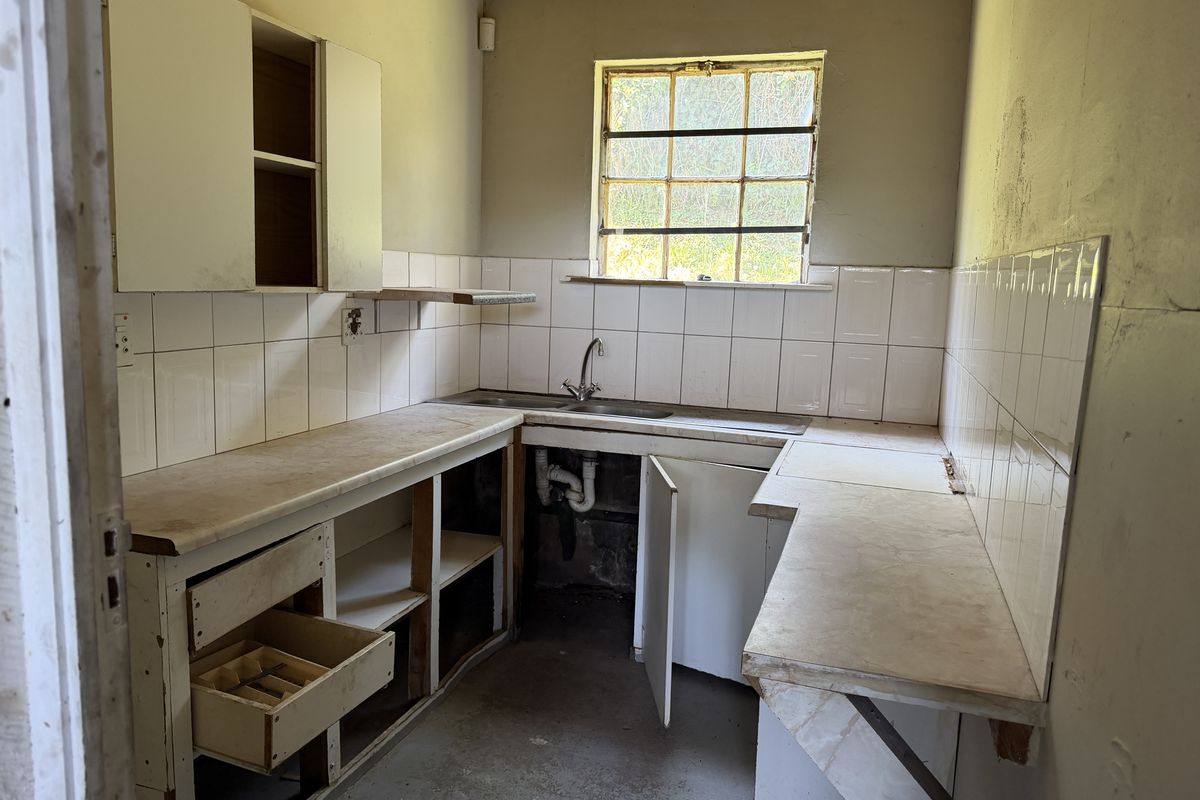 A dated kitchen area featuring original cabinetry, laminate countertops, and a stainless steel sink, requiring significant renovation and cosmetic updates.