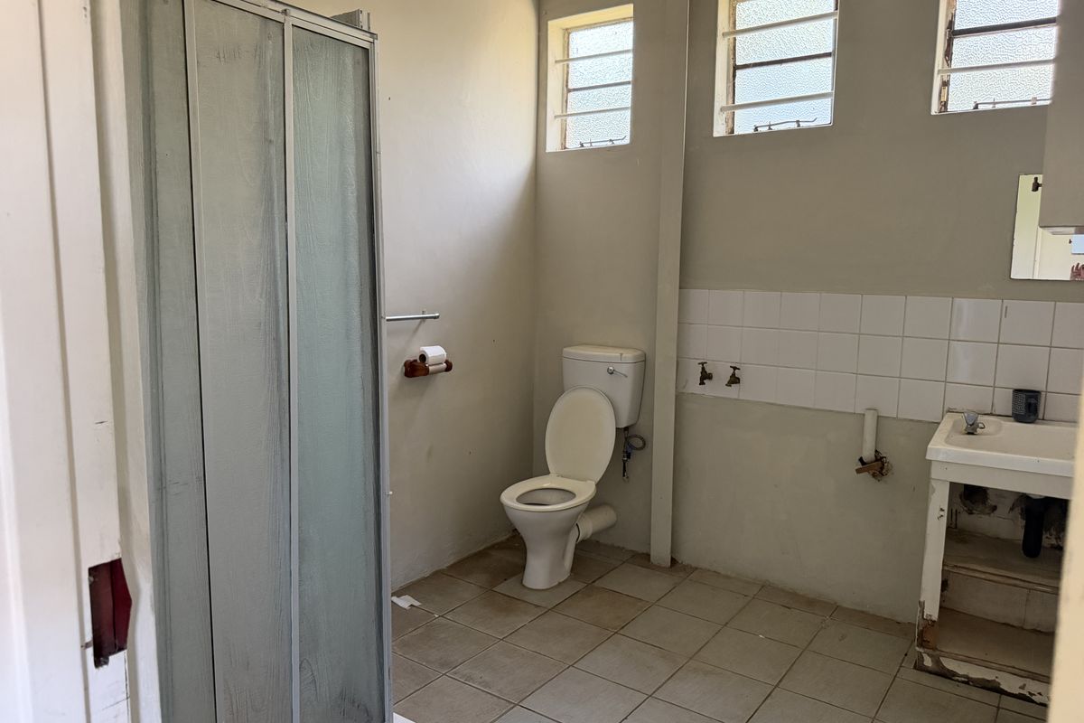 A dated bathroom featuring a shower cubicle, toilet, and pedestal basin, requiring renovation to update the finishes and address exposed plumbing.