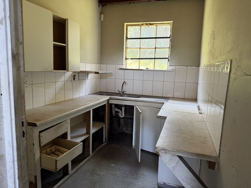 A dated kitchen area featuring original cabinetry, laminate countertops, and a stainless steel sink, requiring significant renovation and cosmetic updates.