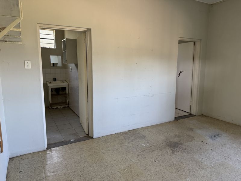 An empty industrial hallway featuring worn tiled flooring and access to a small washroom area with a wall-mounted basin.