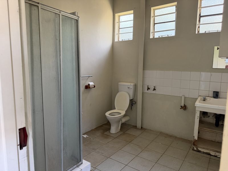 A dated bathroom featuring a shower cubicle, toilet, and pedestal basin, requiring renovation to update the finishes and address exposed plumbing.