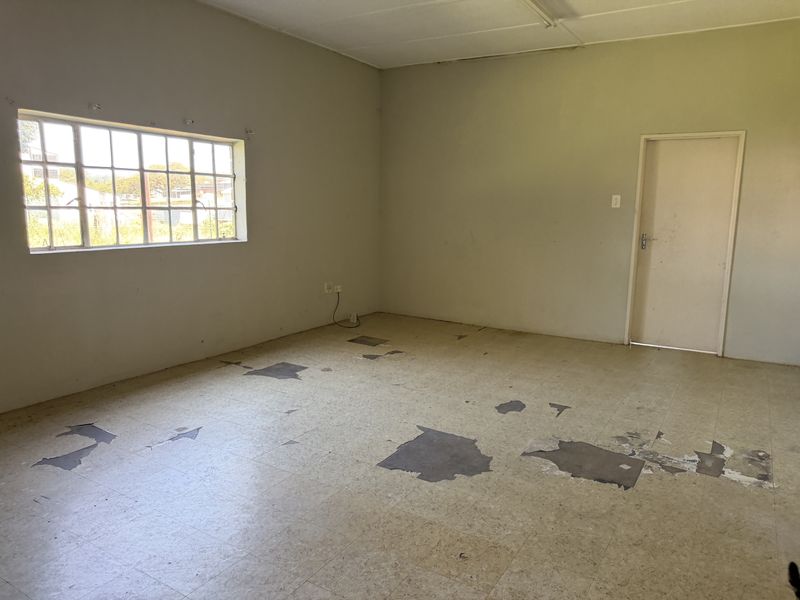 An empty industrial office space featuring a grid window and worn vinyl flooring in need of refurbishment.