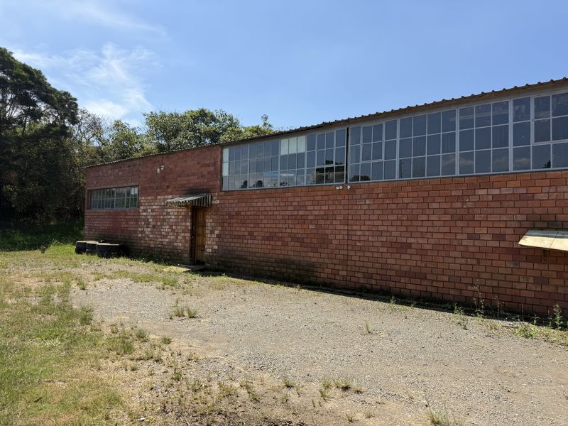 Exterior view of an industrial building featuring exposed brick walls, large steel-framed windows, and an adjacent gravel yard area.