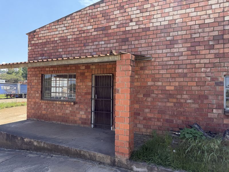 Industrial building exterior featuring exposed brick facade, a covered concrete porch, and a secure metal entrance gate.