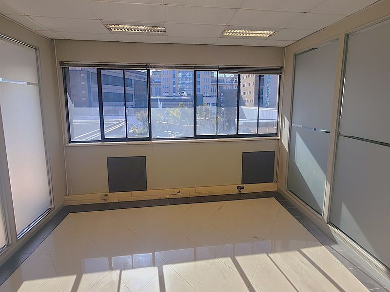 A bright, empty office space featuring tiled flooring, suspended ceilings with recessed lighting, and frosted glass partitions, offering a clean professional environment.