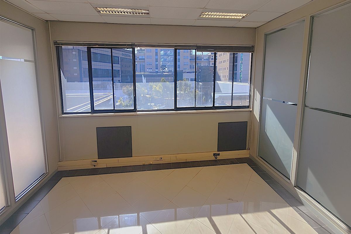 A bright, empty office space featuring tiled flooring, suspended ceilings with recessed lighting, and frosted glass partitions, offering a clean professional environment.