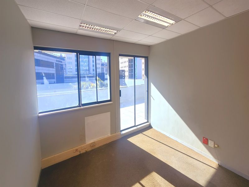 A vacant office space featuring a suspended ceiling, recessed lighting, carpet flooring, and access to an outdoor area through a sliding glass door.