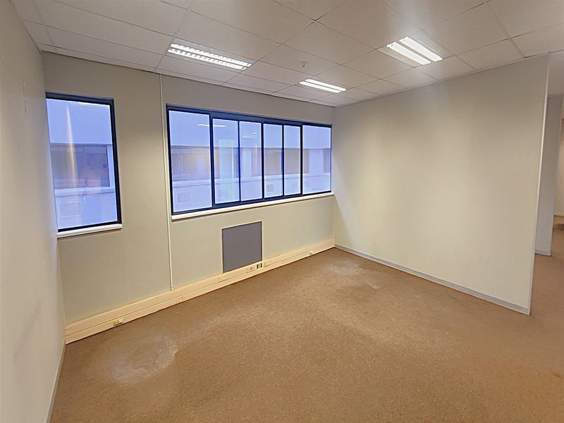 An empty office space featuring a suspended ceiling, recessed lighting, and carpeted flooring with integrated skirting trunking for electrical and data connectivity.