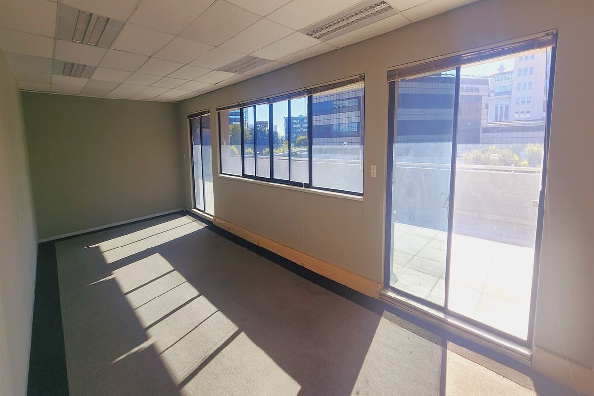 A bright, empty office space featuring a suspended ceiling, carpeted flooring, and large sliding glass doors providing access to an outdoor balcony area.