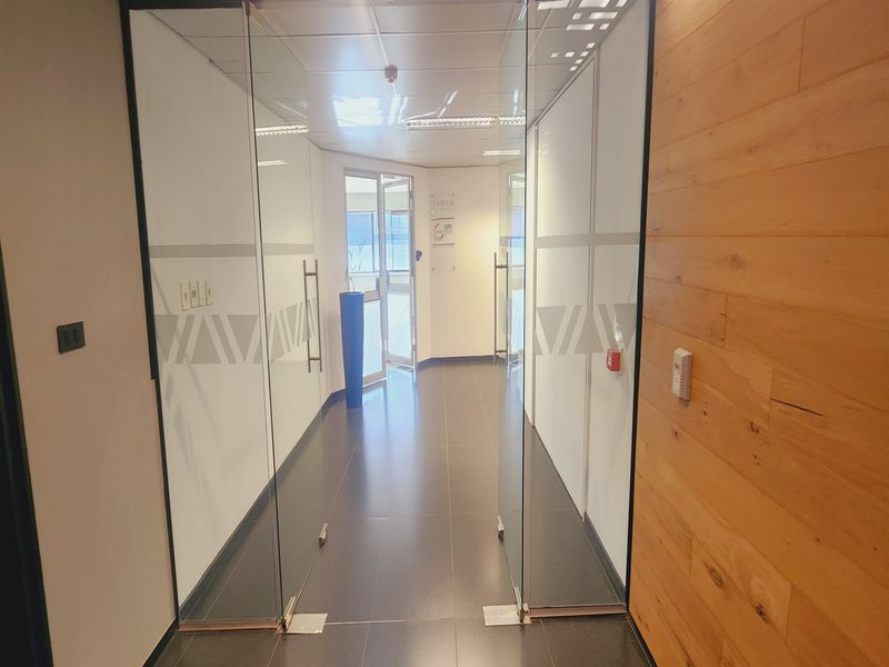 A modern office entrance featuring glass partition doors, tiled flooring, and a combination of white walls and wood paneling accents.