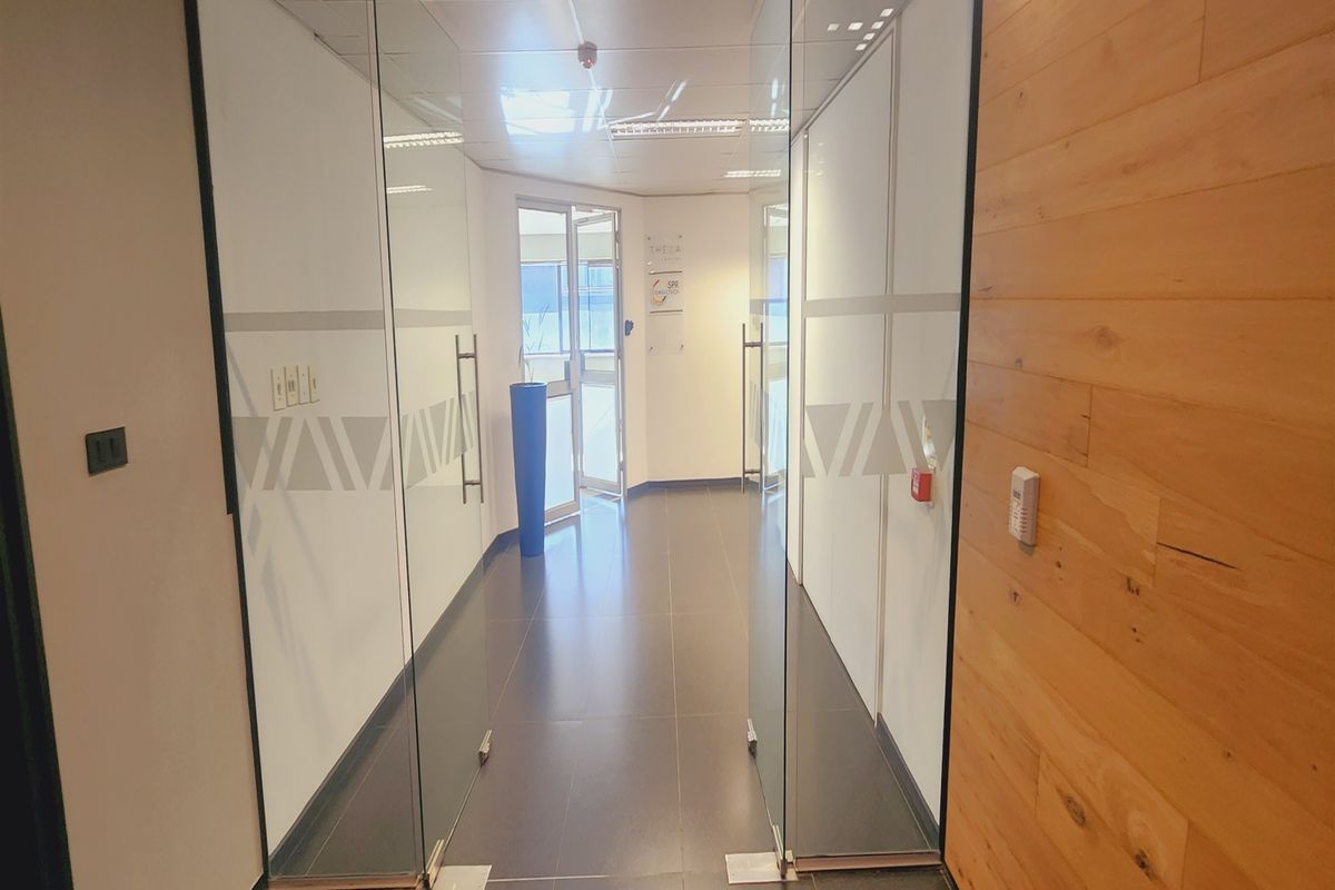 A modern office entrance featuring glass partition doors, tiled flooring, and a combination of white walls and wood paneling accents.