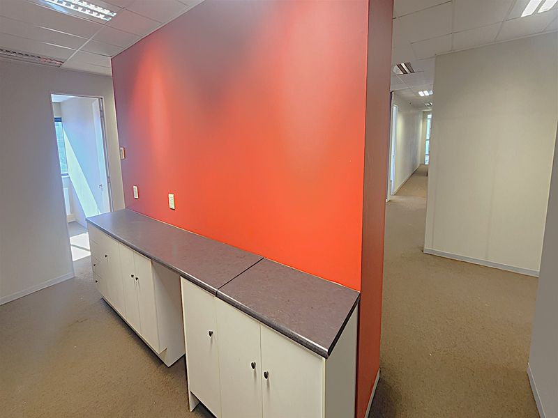 An empty office space featuring built-in cabinetry with a laminate countertop, suspended ceiling, and neutral carpet flooring.