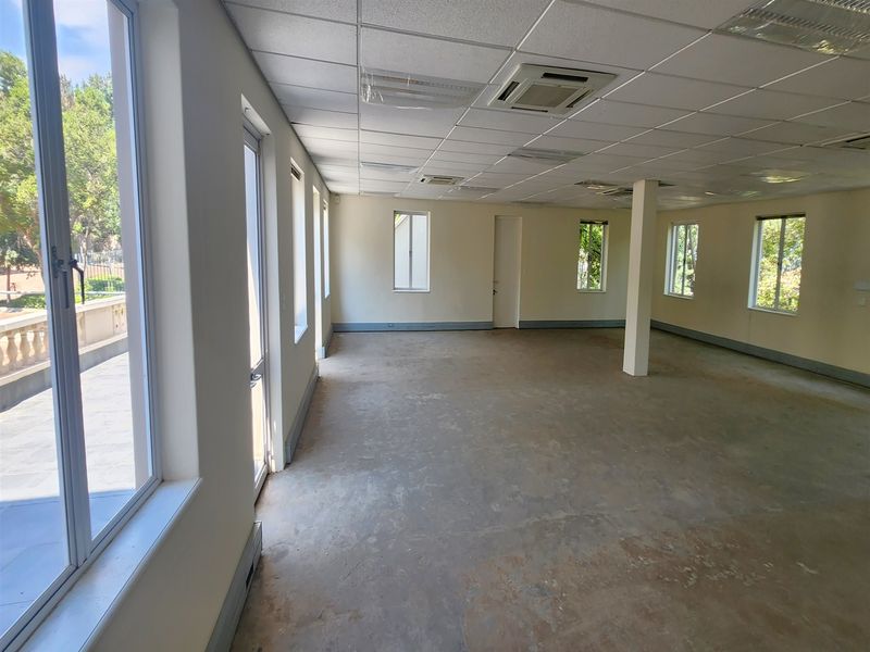 Spacious, empty office area featuring a suspended ceiling, recessed lighting, central air conditioning, and large windows providing ample natural light.