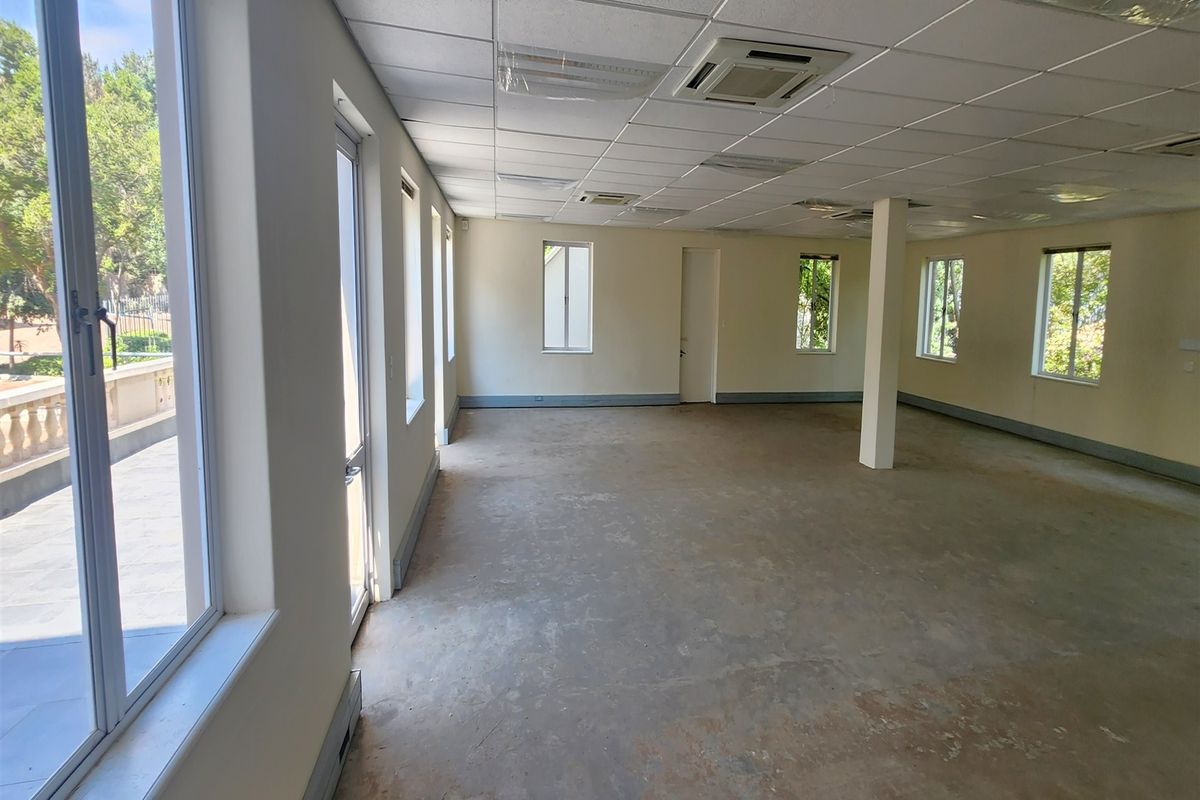 Spacious, empty office area featuring a suspended ceiling, recessed lighting, central air conditioning, and large windows providing ample natural light.