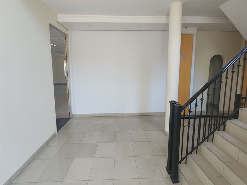 Spacious office entrance foyer featuring tiled flooring, a central structural column, and a staircase with a decorative wrought iron balustrade.
