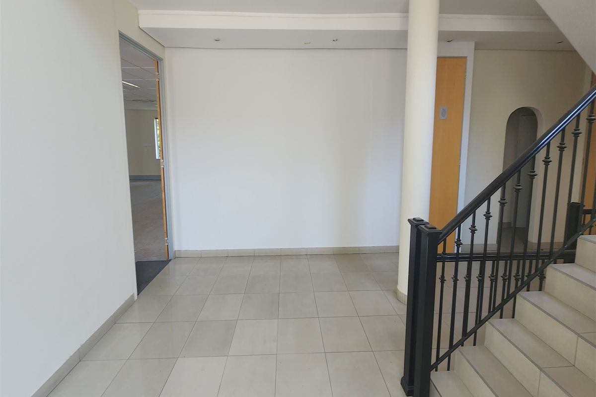 Spacious office entrance foyer featuring tiled flooring, a central structural column, and a staircase with a decorative wrought iron balustrade.