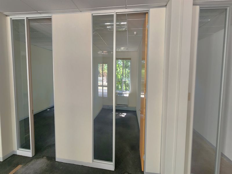 Empty office space featuring glass partition walls, suspended ceilings, and carpet flooring, providing a clean and functional layout for professional use.