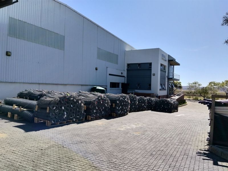 Industrial facility featuring a large warehouse section with corrugated metal cladding and an adjacent multi-level office block with paved driveway access.