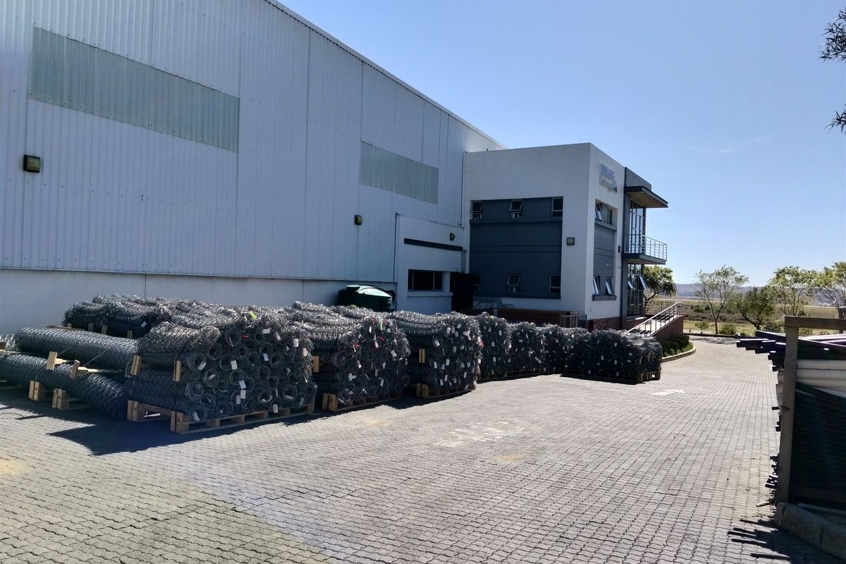 Industrial facility featuring a large warehouse section with corrugated metal cladding and an adjacent multi-level office block with paved driveway access.