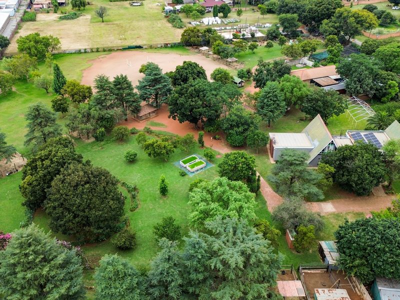 Aerial view of a spacious small holding property featuring extensive landscaped gardens, mature trees, and multiple structures with solar panel installations.