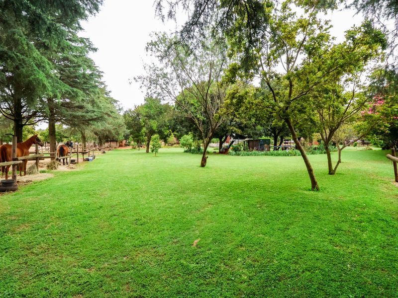 Expansive, well-maintained garden area featuring mature trees and secure post and rail fencing, suitable for equestrian use.