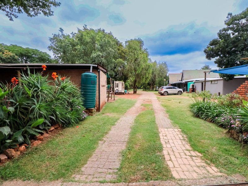A view of the property entrance featuring a brick driveway, established garden, and a water storage tank alongside the outbuilding.