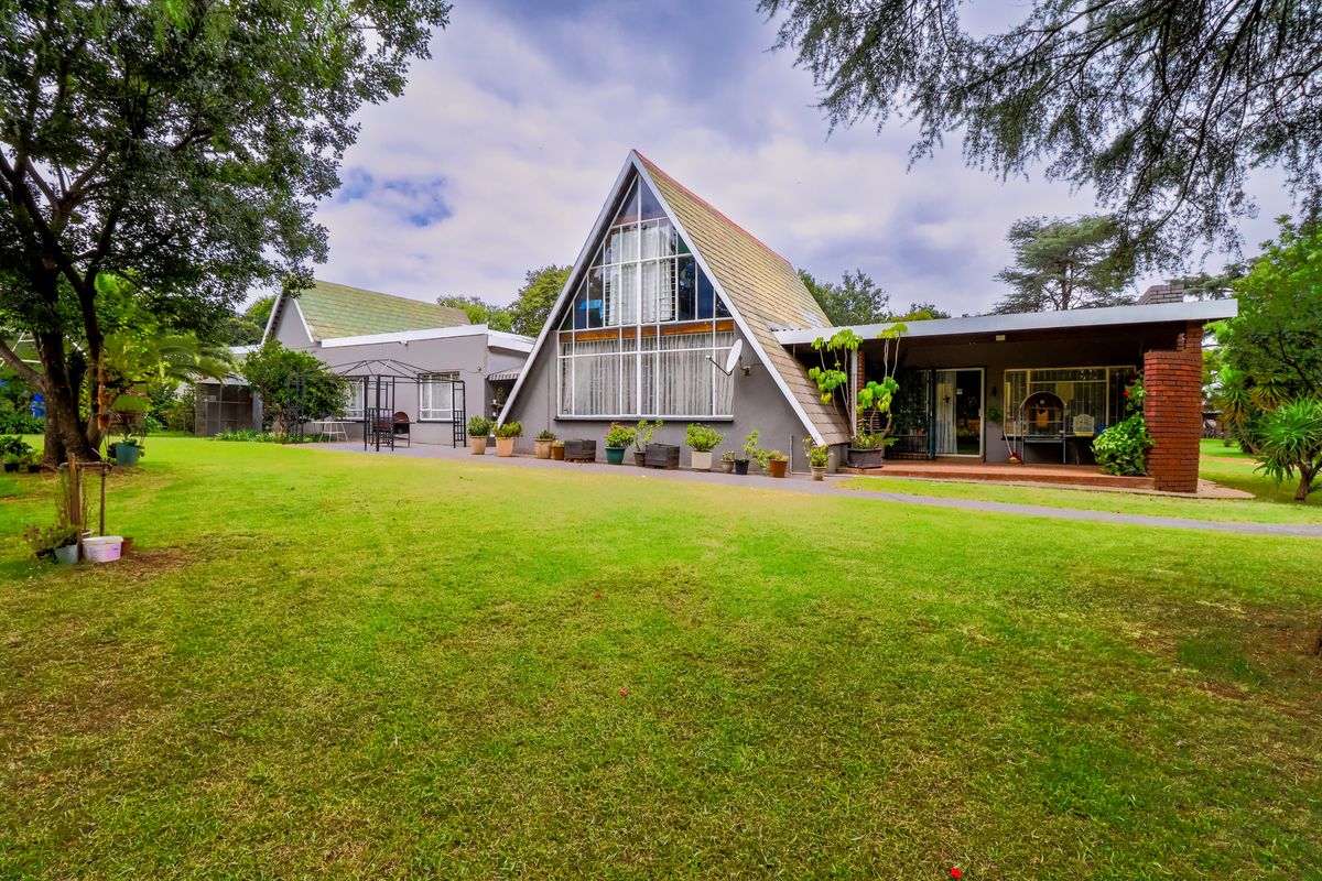 Rear view of a unique A-frame style home featuring a spacious lawn, mature trees, and a covered patio area.