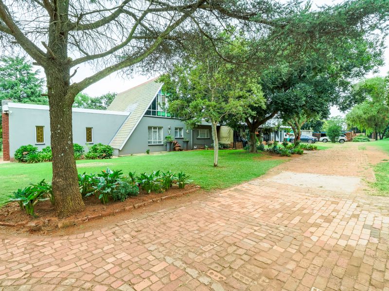 Front view of a small holding property featuring a unique A-frame architectural design, a brick driveway, and established garden landscaping.