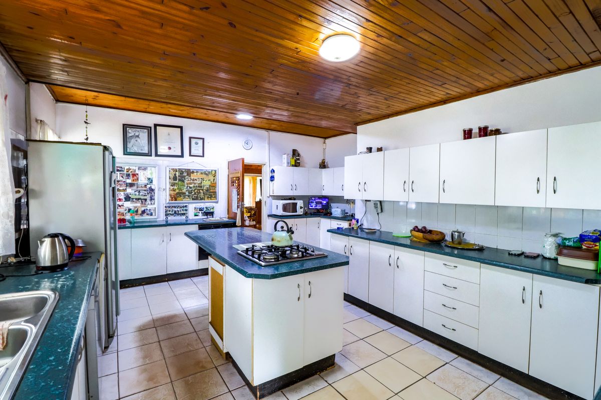Spacious kitchen featuring a central island with a gas hob, ample built-in cabinetry, double sink, and a distinctive timber-clad ceiling.