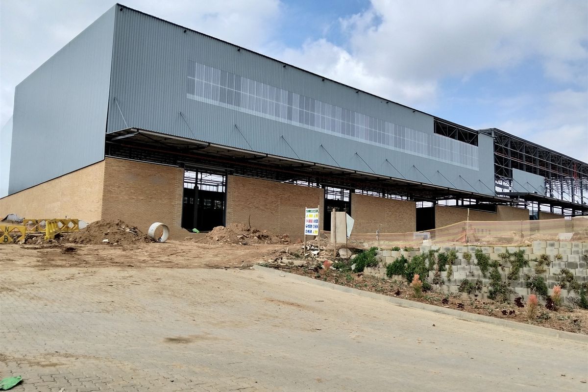 Exterior view of a large industrial warehouse facility currently under construction, featuring brick and metal cladding with an unfinished site area.