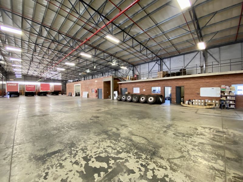 Spacious industrial warehouse featuring high ceilings with exposed steel trusses, sprinkler system, and durable concrete flooring, suitable for logistics or manufacturing operations.