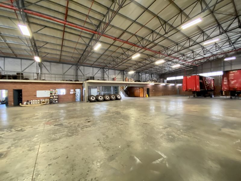 Spacious industrial warehouse featuring high ceilings with exposed steel trusses, a mezzanine level, and durable concrete flooring suitable for storage or manufacturing operations.