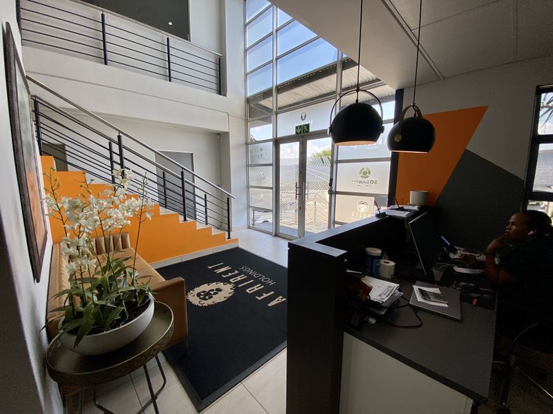 Modern industrial reception area featuring a double-volume glass entrance, sleek metal staircase, and a professional built-in reception desk.