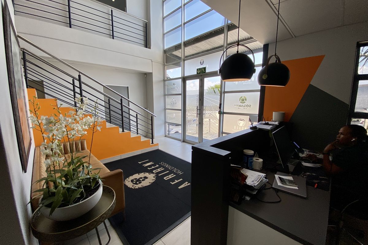 Modern industrial reception area featuring a double-volume glass entrance, sleek metal staircase, and a professional built-in reception desk.