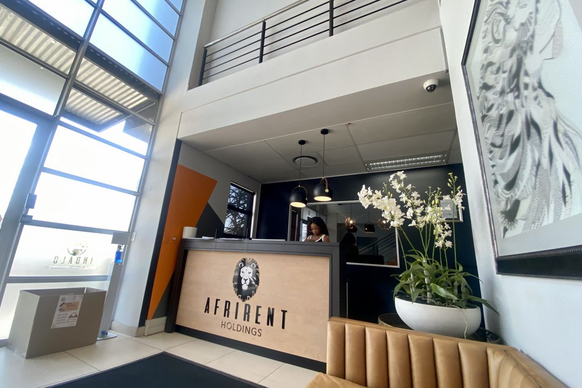 Modern industrial reception area featuring double volume ceilings, a mezzanine level with metal balustrades, and a large glass facade providing ample natural light.