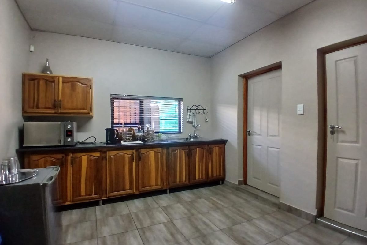 A functional kitchen area featuring wooden cabinetry, tiled flooring, and a stainless steel sink, providing a practical workspace for commercial use.