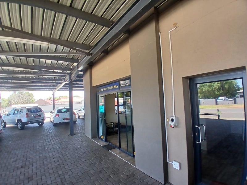 Commercial exterior view featuring a covered parking area with paved driveway and glass entrance doors to the office space.
