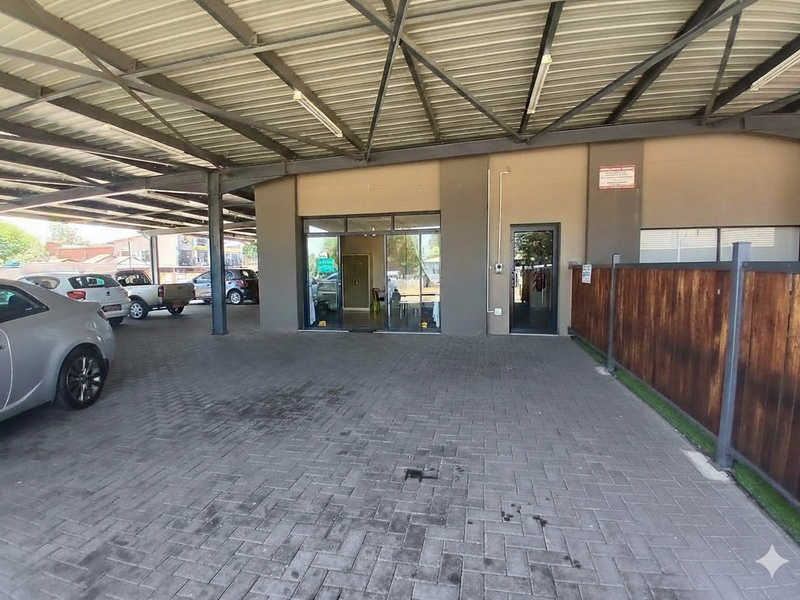 Commercial property exterior featuring a large covered parking area with steel roofing, paved driveway, and aluminum-framed glass entrance doors.