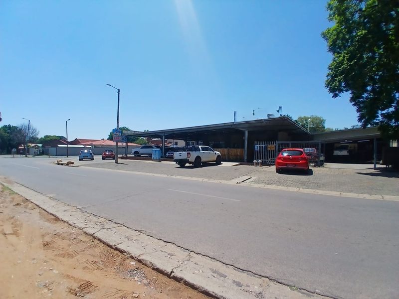 Street-facing view of a commercial property featuring a paved driveway, metal carport structure, and perimeter security fencing.
