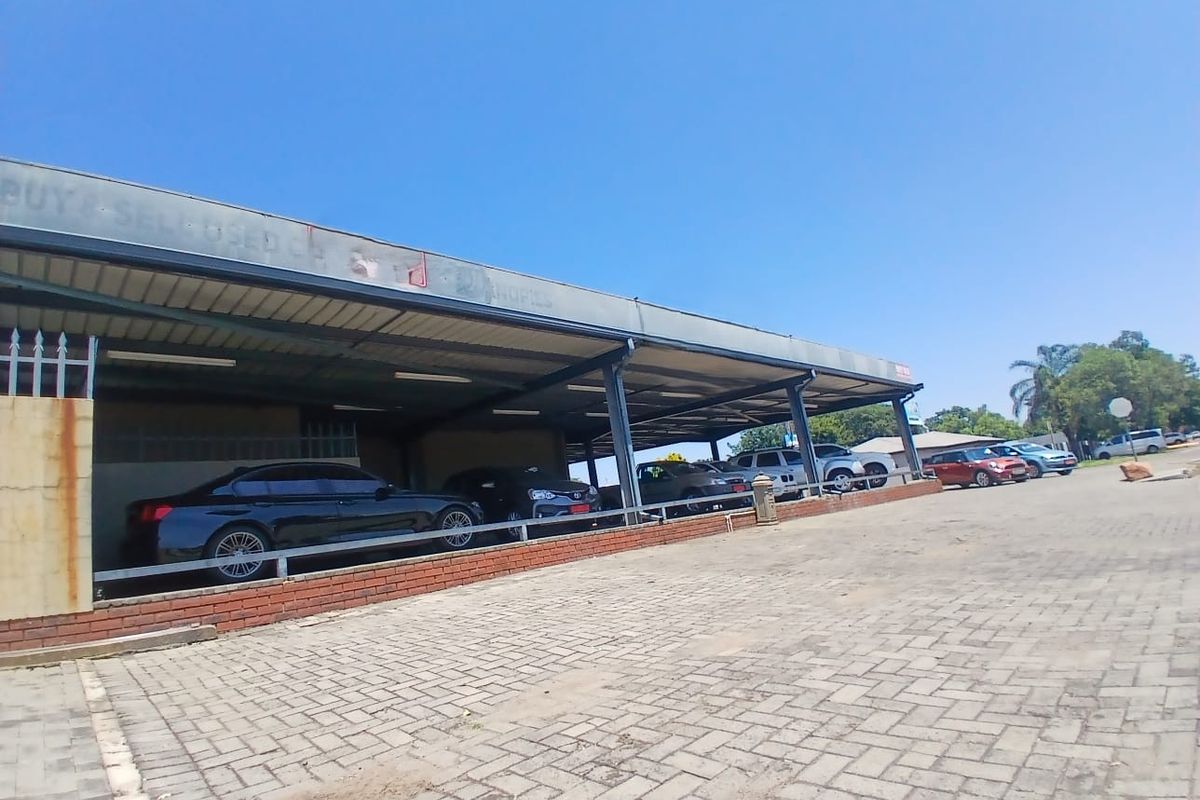 Commercial property featuring a large covered parking area with brick paving and a steel-framed structure, suitable for vehicle display or client parking.