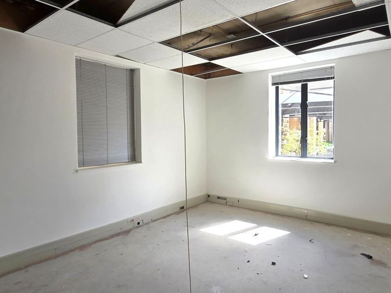An empty office space featuring large windows with blinds and a partially damaged suspended ceiling, requiring renovation to restore the interior finishes.