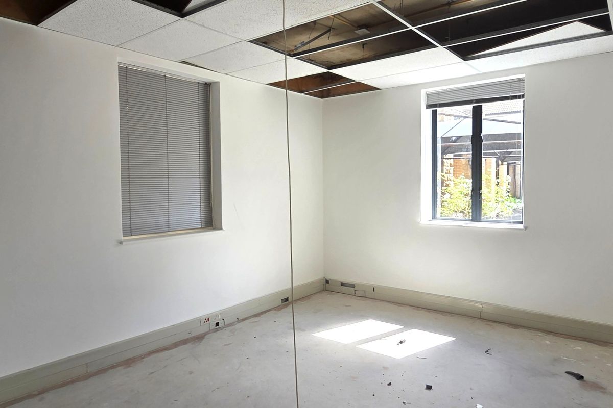 An empty office space featuring large windows with blinds and a partially damaged suspended ceiling, requiring renovation to restore the interior finishes.