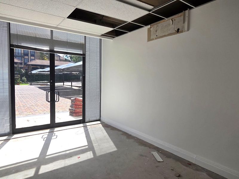 An empty office space featuring large glass doors, unfinished flooring, and a partially damaged suspended ceiling, offering a blank canvas for renovation.