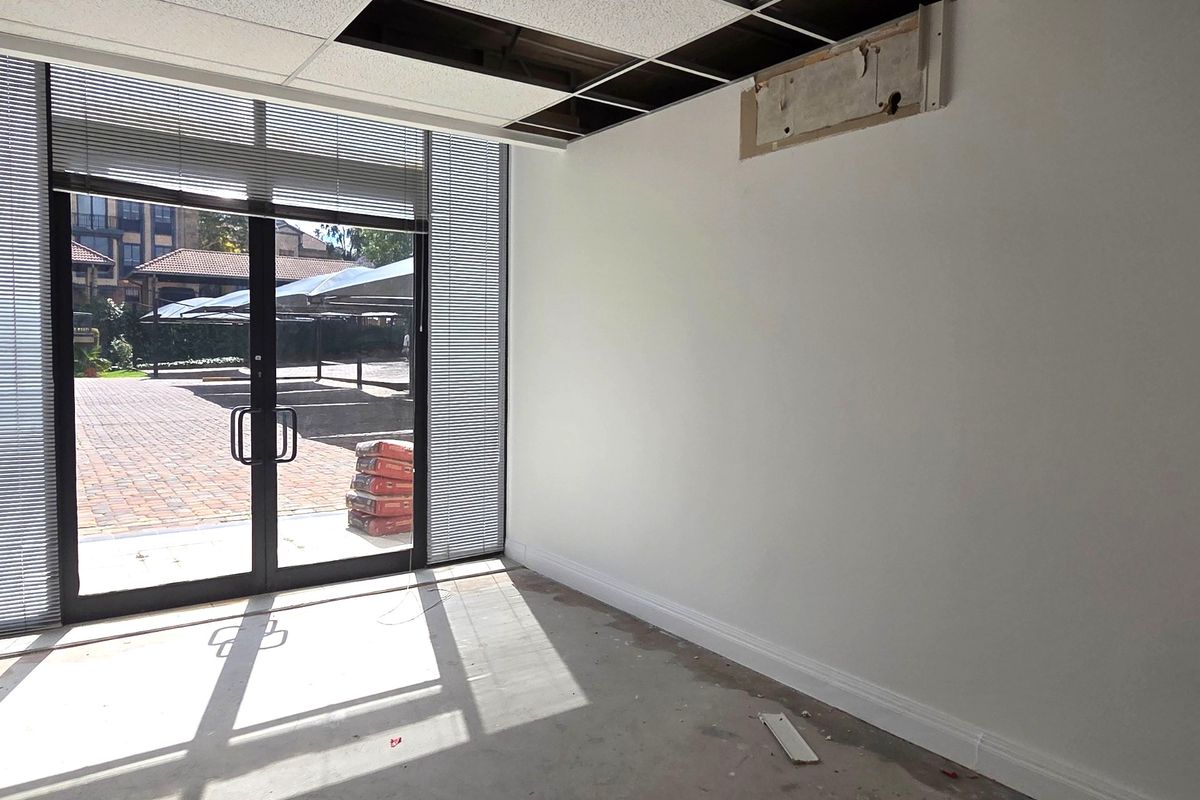 An empty office space featuring large glass doors, unfinished flooring, and a partially damaged suspended ceiling, offering a blank canvas for renovation.