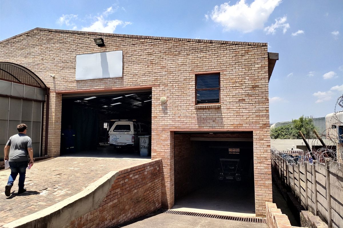 Industrial property exterior featuring a brick facade, large roller shutter access, and a dedicated underground parking entrance with perimeter security fencing.