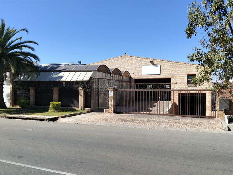 Front exterior view of an industrial property featuring a brick facade, secure sliding gate, razor wire fencing, and a curved polycarbonate awning over the entrance.