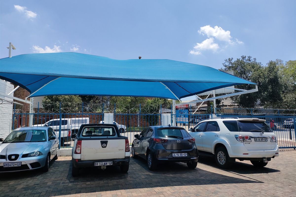 Paved industrial parking area featuring a large blue shade cloth structure and secure perimeter fencing with razor wire.