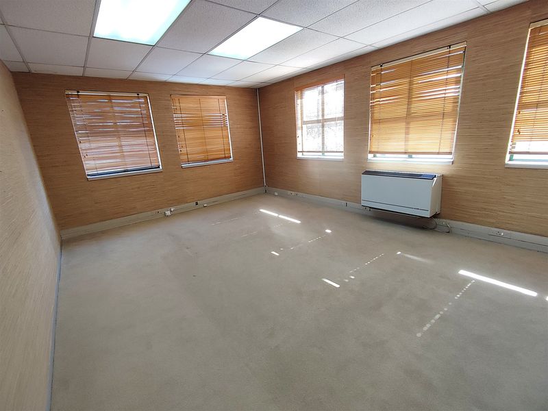 A spacious, empty office featuring wood-effect wall paneling, carpeted flooring, recessed ceiling lighting, and wall-mounted climate control units.