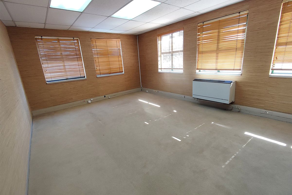 A spacious, empty office featuring wood-effect wall paneling, carpeted flooring, recessed ceiling lighting, and wall-mounted climate control units.