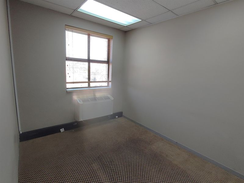 A vacant office space featuring a drop ceiling, recessed lighting, an integrated HVAC unit, and carpet flooring in need of replacement.